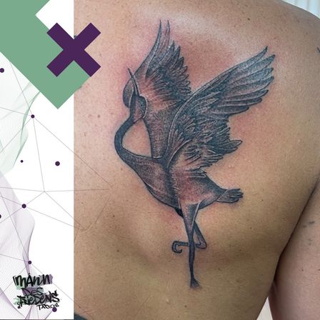 Ein detailliertes Tattoo eines fliegenden Störches auf der Schulter einer Person. Das Tattoo ist schwarz und grau, mit komplizierter Schattierung und Federdetails.