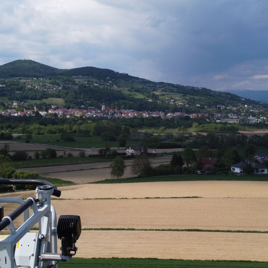 Ein Feuerwehrmann steht in einem Kran und überblickt eine ländliche Landschaft mit grünen Feldern, entfernten Bergen und einer Stadt.