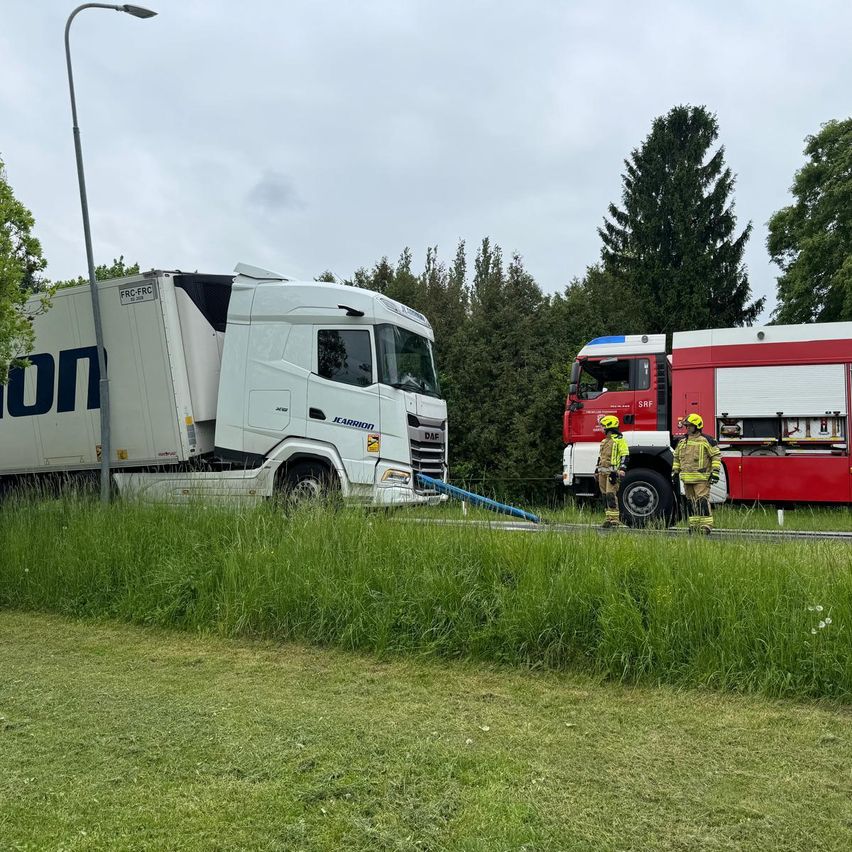 Ein weißer Lkw ist am Straßenrand geparkt, mit einem Feuerwehrwagen in der Nähe. Zwei Feuerwehrleute stehen neben dem Feuerwehrwagen.