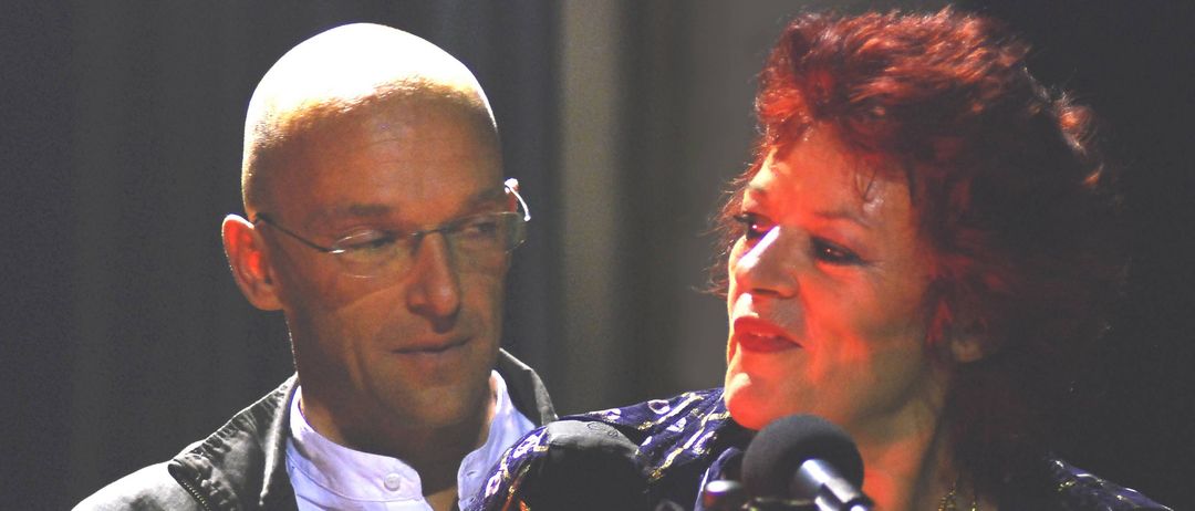 Ein Mann mit Brille und eine Frau mit roten Haaren singen auf der Bühne mit Mikrofonen.