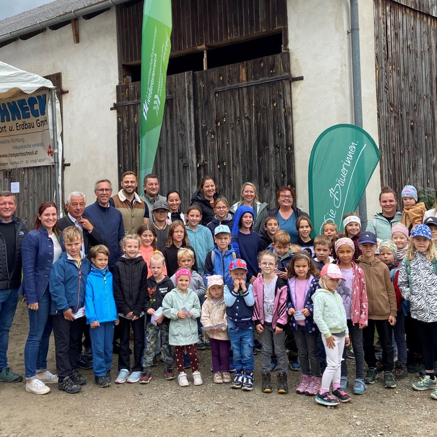 Eine Gruppe von Erwachsenen und Kindern posiert für ein Foto vor einer Scheune, einige halten Urkunden in der Hand. Dahinter hängen Banner, eines mit dem Wort 'Abenteuer'.