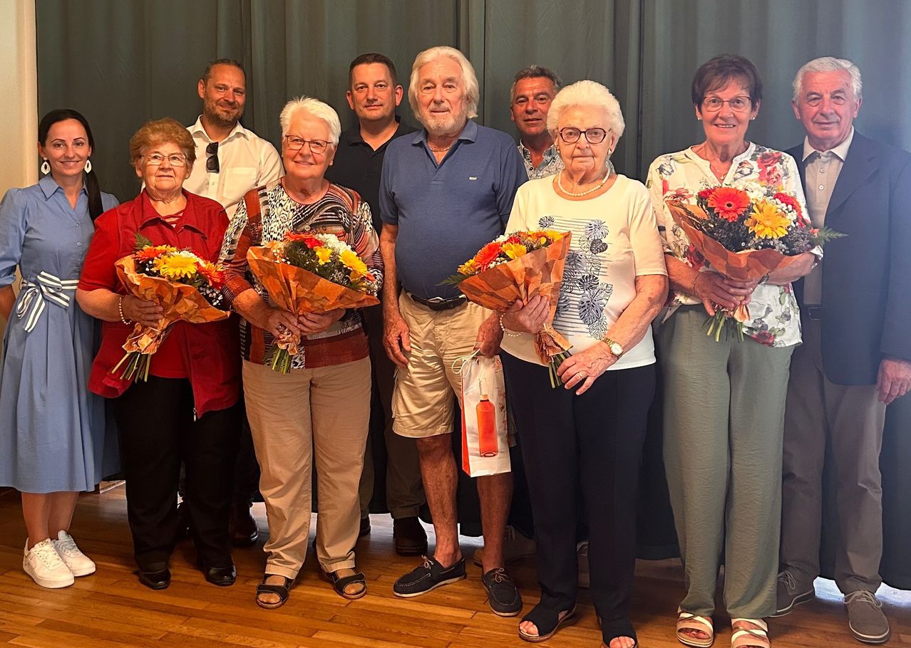 Eine Gruppe älterer Menschen und jüngerer Erwachsener lächelt für ein Foto und hält Blumensträuße.