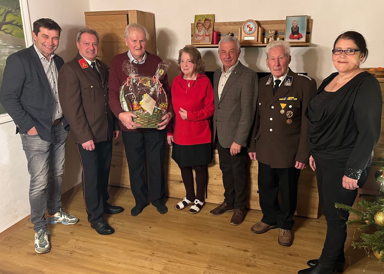 Sechs Personen stehen in einem Raum mit Holzboden. Eine Person hält einen Korb. Die Gruppe umfasst Personen in Militäruniformen.