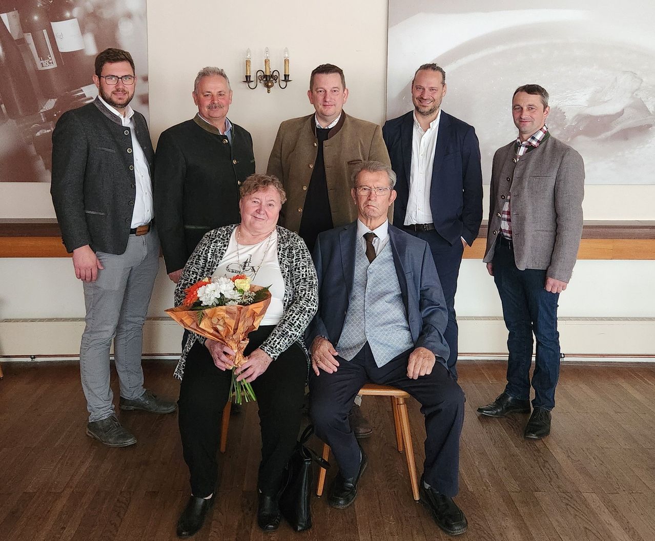 Sieben Männer und eine Frau stehen zusammen. Eine Frau hält einen Blumenstrauß. Sie lächeln und scheinen für ein Foto zu posieren.