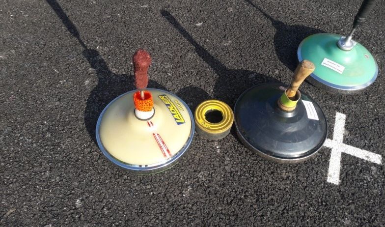 Drei Verkehrskegel stehen auf einer Straße mit einem gelben und einem grünen Kegel vor einem weißen Buchstaben X.