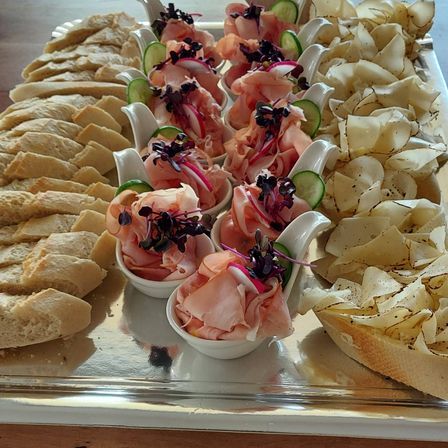 Ein Tablett mit verschiedenen Speisen umfasst Fleischscheiben, Brot und Pommes, alles kunstvoll mit Gurken und Blumen garniert.