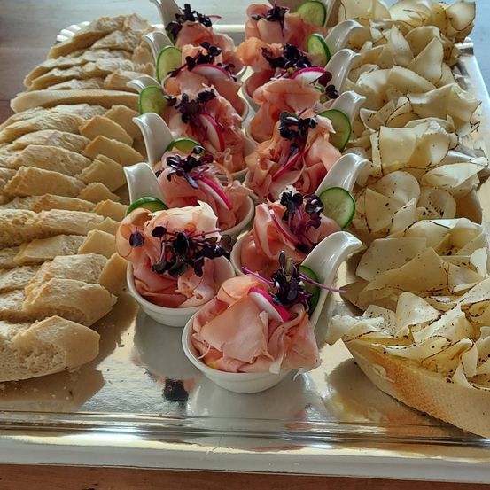 Ein Tablett mit verschiedenen Speisen umfasst Fleischscheiben, Brot und Pommes, alles kunstvoll mit Gurken und Blumen garniert.