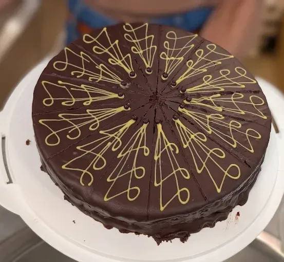 Ein Schokoladenkuchen mit gelben Wirbeln auf einem weißen Teller, die Hand von jemandem ist im Hintergrund sichtbar.