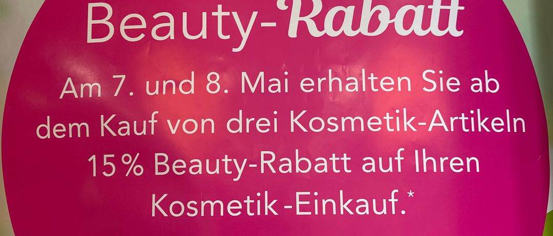 Ein Plakat bewirbt einen Beauty-Rabatt. Am 7. und 8. Mai erhalten Sie beim Kauf von drei Kosmetik-Artikeln 15% Rabatt auf Ihren Kosmetik-Einkauf. Das Poster hat ein pinkes kreisförmiges Design mit einem Blumensymbol.