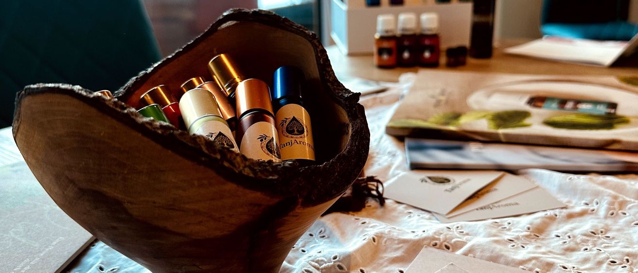 Eine hölzerne Schüssel mit verschiedenen ätherischen Ölen und beschrifteten Flaschen, auf einem Tisch mit einem Spitzentuch. Ein Leitfaden mit dem Titel 'Your Tox Guide' ist teilweise sichtbar.