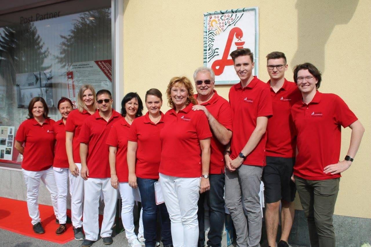 Eine Gruppe von Menschen in roten Poloshirts und weißen Hosen steht vor einem Gebäude mit einem Schild, das 'A' steht.