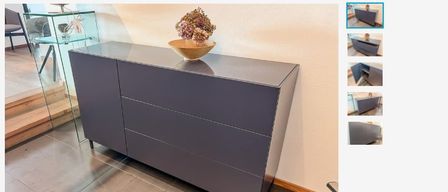 A gray sideboard with three drawers and a bowl of flowers on top. A glass table and a chair are visible on the left.