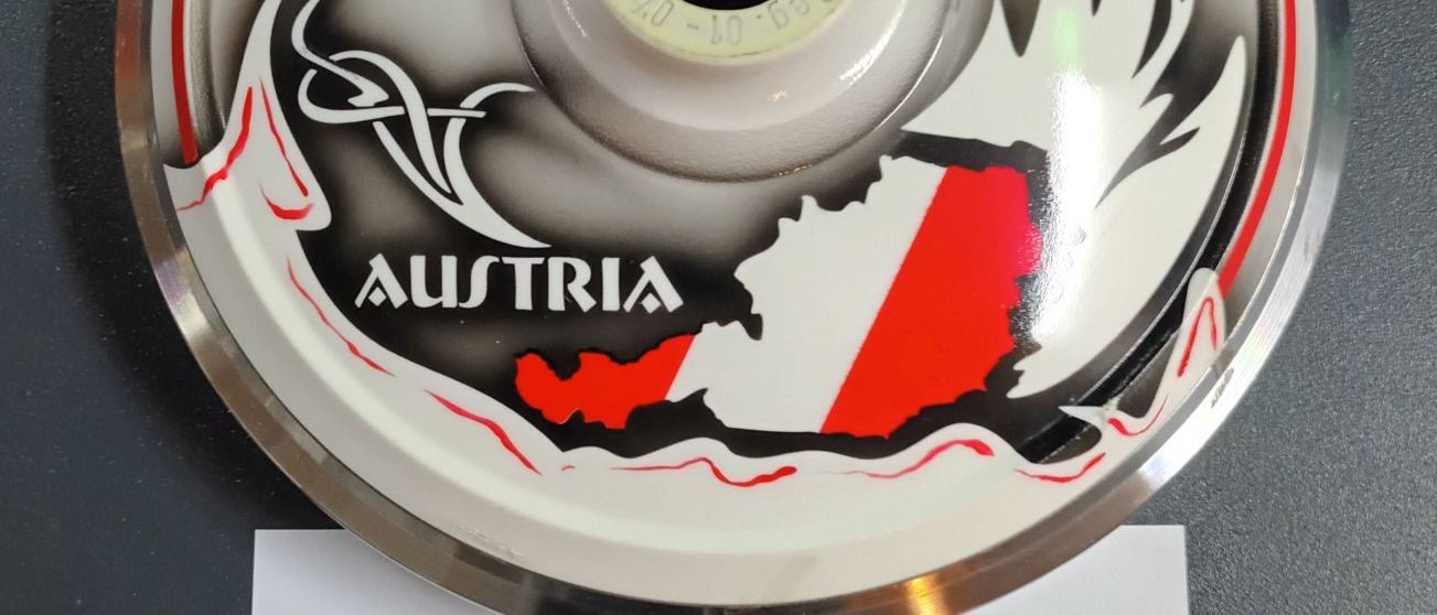 Eine runde, silberne Medaille zeigt ein Design der Karte österreichs mit dem Text 'Austria'. Darunter befindet sich ein roter Aufkleber mit weissem Text 'ASKÖ'.