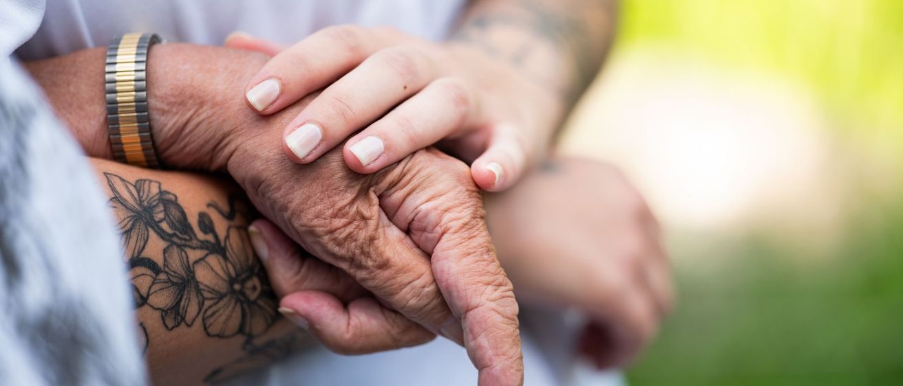 Ein Nahaufnahme einer Hand mit Blumen-Tattoo, die von einer anderen Person mit tätowierten Armen gehalten wird.