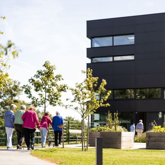 Eine Gruppe älterer Menschen geht in einem Park, im Hintergrund steht ein modernes Gebäude.