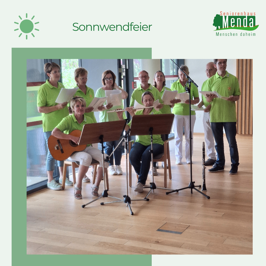 Eine Gruppe von Menschen in grünen Hemden und Hosen tritt mit Instrumenten in einem Raum mit Holzboden auf. Einige stehen, andere sitzen auf Stühlen.