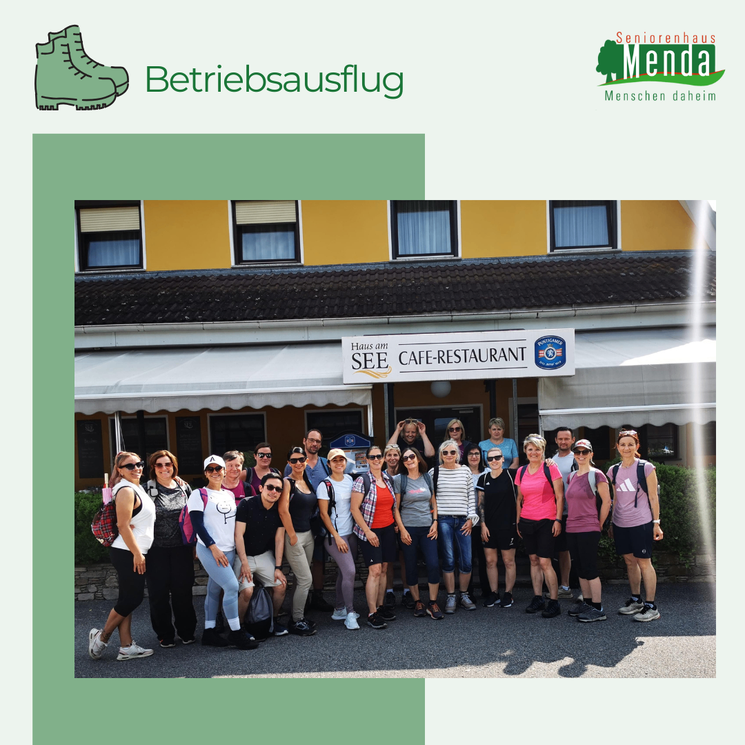 Eine Gruppe von Menschen steht vor einem Gebäude mit einem Schild, das 'HAUS AM SEE CAFE-RESTAURANT' besagt. Sie tragen Freizeitkleidung und einige haben Hüte auf. Das Gebäude hat gelbe Wände und weiße Vordächer.