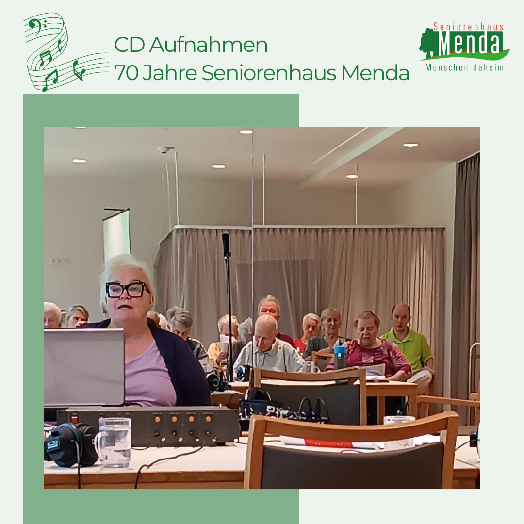Eine Gruppe älterer Menschen sitzt in einem Besprechungsraum um einen Tisch herum, eine Frau mit Brille nimmt mit Laptop und Ausrüstung auf.