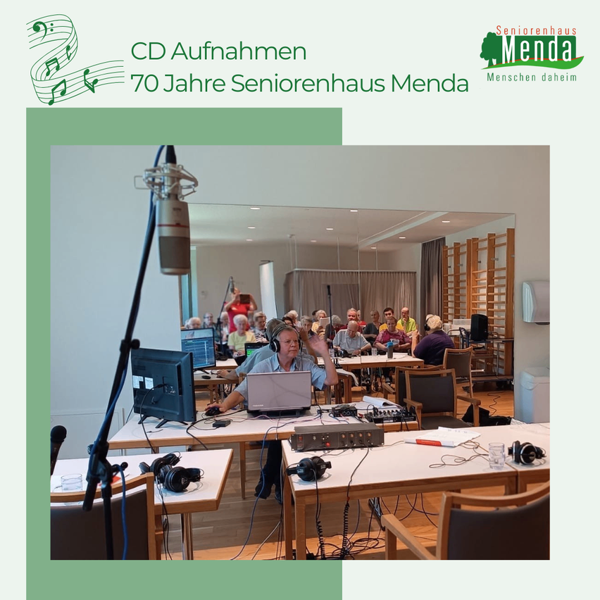 Eine Gruppe von Menschen nimmt eine CD in einem Studio mit Mikrofonen und Laptops auf. Das Studio hat Holzböden und Tische. Das Bild trägt den Titel '70 Jahre Seniorenhaus Menda'.