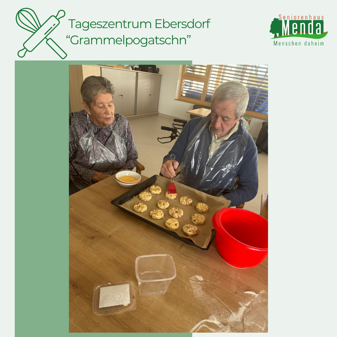 Zwei ältere Personen backen im Tageszentrum Ebersdorf. Der Mann dekoriert Kekse mit einem Pinsel, während die Frau zuschaut. Kekse liegen auf einem Tablett auf dem Tisch.