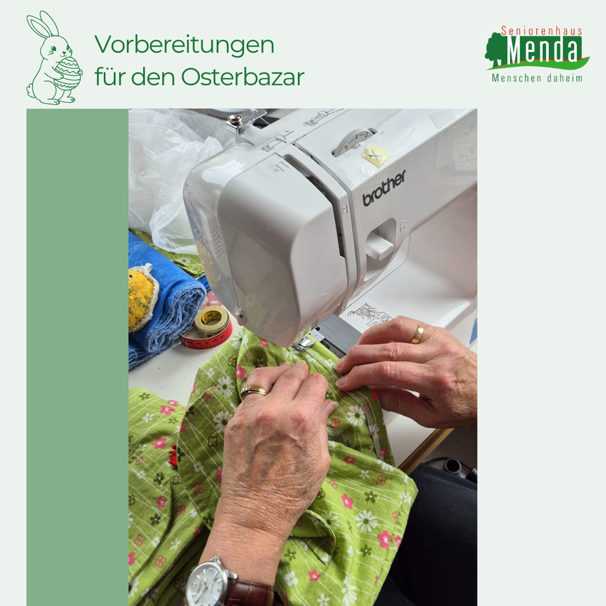 Eine ältere Person näht an einer Brother-Nähmaschine. Im Hintergrund befinden sich farbenfrohe Stoffe, ein Maßband und ein blauer Stoff. Das Bild ist Teil des Seniorenhauses Menda.
