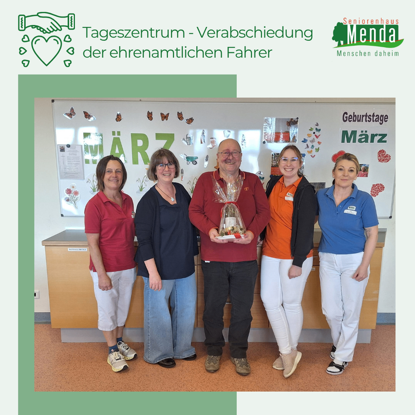 Fünf Personen stehen in einer Reihe vor einer Wand mit Geburtstagsdekoration. Der Mann in der Mitte hält einen Geschenkkorb.