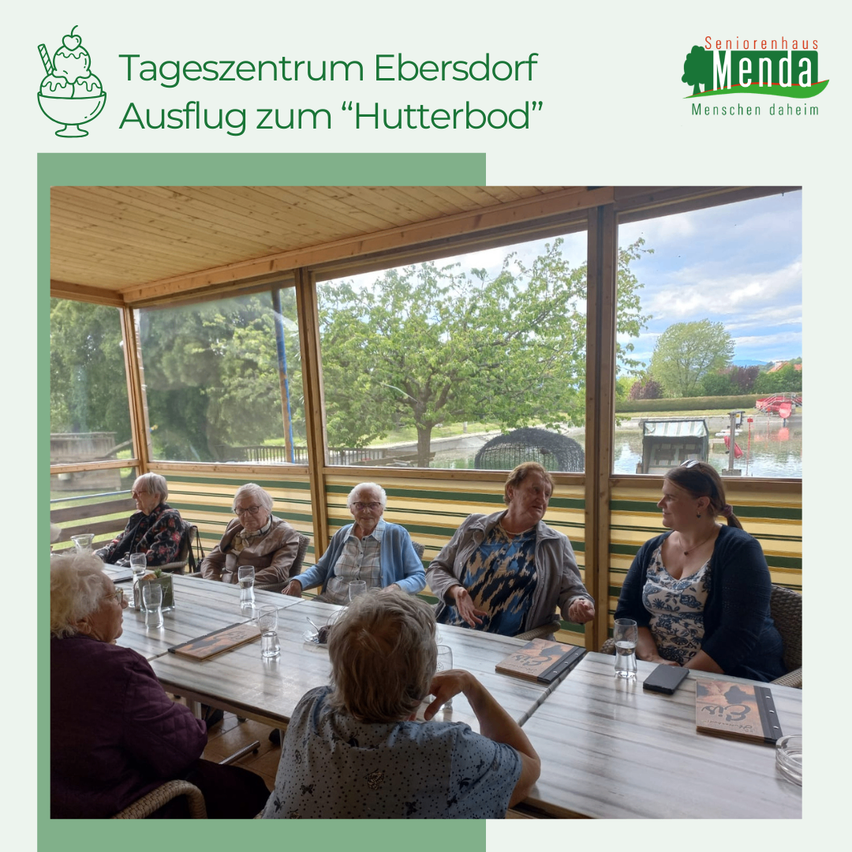 Ein Essbereich im Freien mit Tischen und Stühlen, ältere Menschen sitzen herum, ein Glasfenster mit Blick auf einen Baum und einen See.
