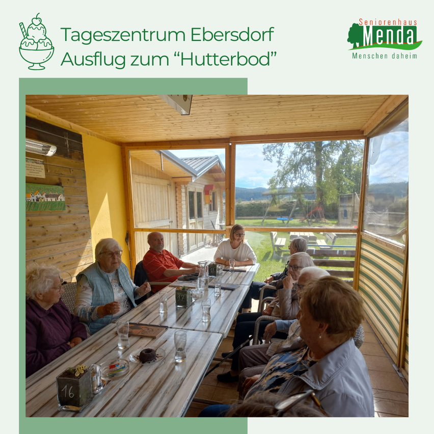 Ältere Frauen sitzen an einem Tisch in einem sonnigen, offenen Café. Eine hält ein Glas Wasser. Das Café blickt auf einen Rasenbereich mit einem Gebäude.