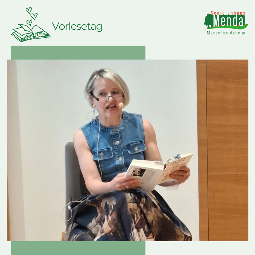 Eine Frau sitzt in einem Stuhl, liest ein Buch und trägt eine Jeansweste und eine Brille. Sie hat ein Mikrofon am Ohr, was darauf hindeutet, dass sie möglicherweise eine Aufnahme macht oder an einer Veranstaltung teilnimmt.