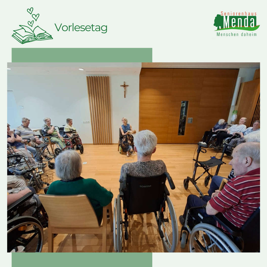 Eine Gruppe älterer Menschen in Rollstühlen versammelt sich in einem Raum, einige sitzend, einige stehend. Eine Frau liest aus einem Buch. Hinter ihr ein Kreuz an der Wand. Der Raum hat Holzböden.