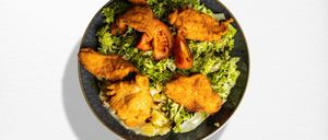 Eine Schüssel gemischter Blattsalat mit knusprigen gebratenen Hühnchenstücken und Tomatenscheiben auf weißem Hintergrund.