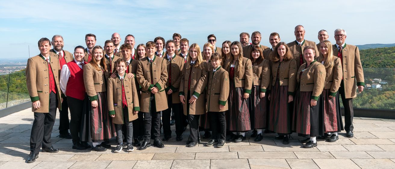 Eine Gruppe von Menschen in traditioneller bayerischer Kleidung, die auf einem Steinboden stehen, lächeln und für ein Foto posieren.