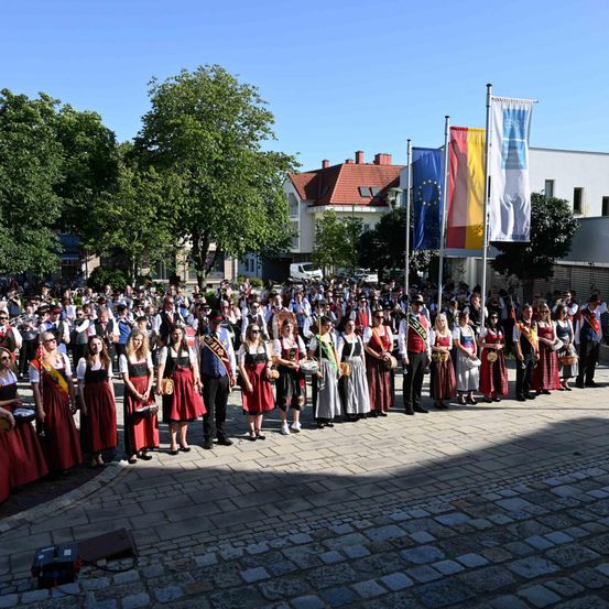 Eine große Gruppe von Menschen in traditioneller bayerischer Kleidung versammelt sich auf einem Stadtplatz, möglicherweise für ein Festival.