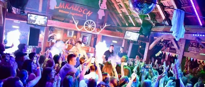 Eine lebhafte Menge genießt Musik in einem lebhaften Nachtclub mit Discokugeln und Neonlichtern, eingefangen in einem Moment der Feier und Energie.