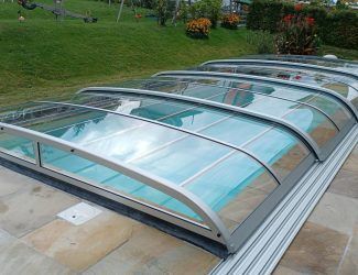 Ein Außenpool mit einer versenkbaren Glasabdeckung, auf einem Steinboden mit einem Rasen im Hintergrund.