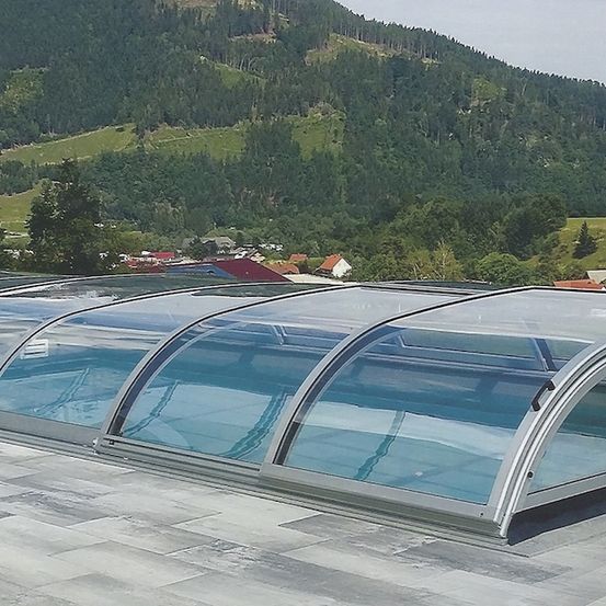 Drei Glasdachverlängerungen über einem Swimmingpool auf einem Dach, mit einem Berg und Häusern im Hintergrund.