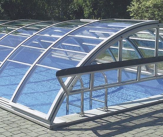 Ein Freischwimmbecken mit einem transparenten, gewölbten Glasdach bedeckt. Das Becken hat einen Metallhandlauf an der Seite.