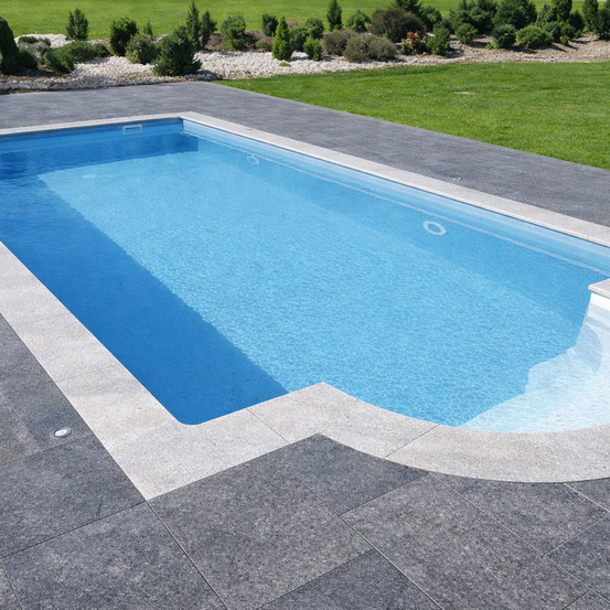 Ein Außenpool mit klarem blauem Wasser und einem Betondeck. Der Pool ist von einer Rasenfläche mit Sträuchern umgeben.