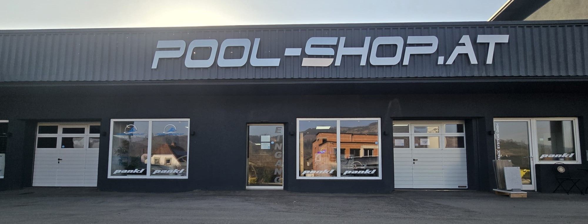 Das Äußere eines Geschäfts mit einem großen Schild, das 'POOL-SHOP' über dem Eingang steht. Zwei Glastüren und drei Fenster zeigen Reflexionen eines Gebäudes und eines Fahrzeugs.