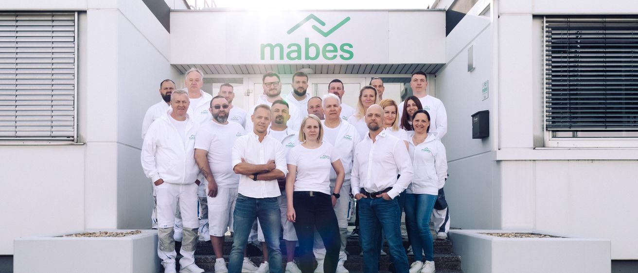 Eine Gruppe von Männern und Frauen in weißen Laborkitteln steht vor einem Gebäude mit dem Namen Mabes.