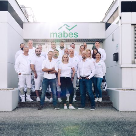 Eine Gruppe von Menschen in weißen Jacken und Hosen steht vor einem Gebäude mit dem Schild mabes oben.