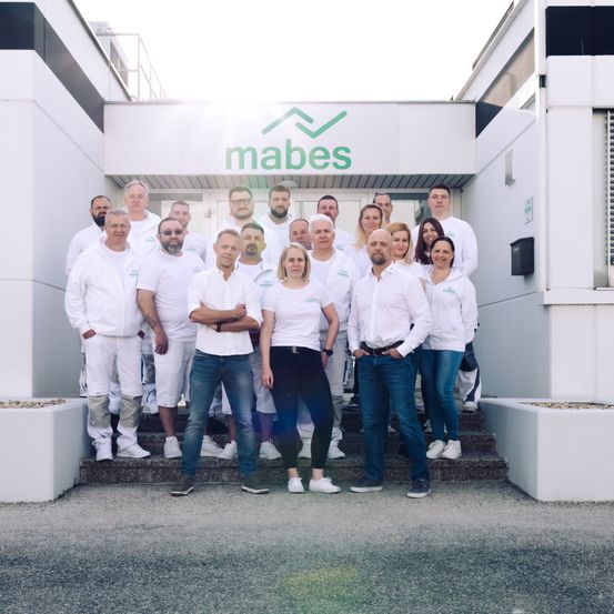 Eine Gruppe von Menschen in weißen Jacken und Hosen steht vor einem Gebäude mit dem Schild mabes oben.