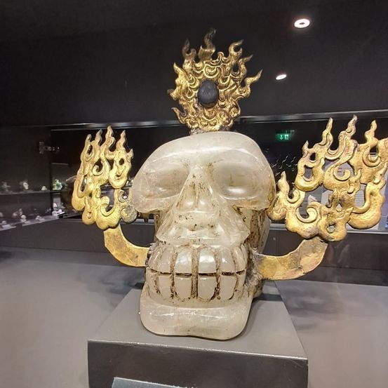 Ein Kristallschädel mit goldenen Verzierungen und einem schwarzen Stein darauf wird in einem Museum ausgestellt.