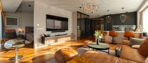 Ein modernes Wohnzimmer mit Holzböden und einem Flachbildfernseher an der Wand. Eine Kristallleuchte hängt an der Decke.
