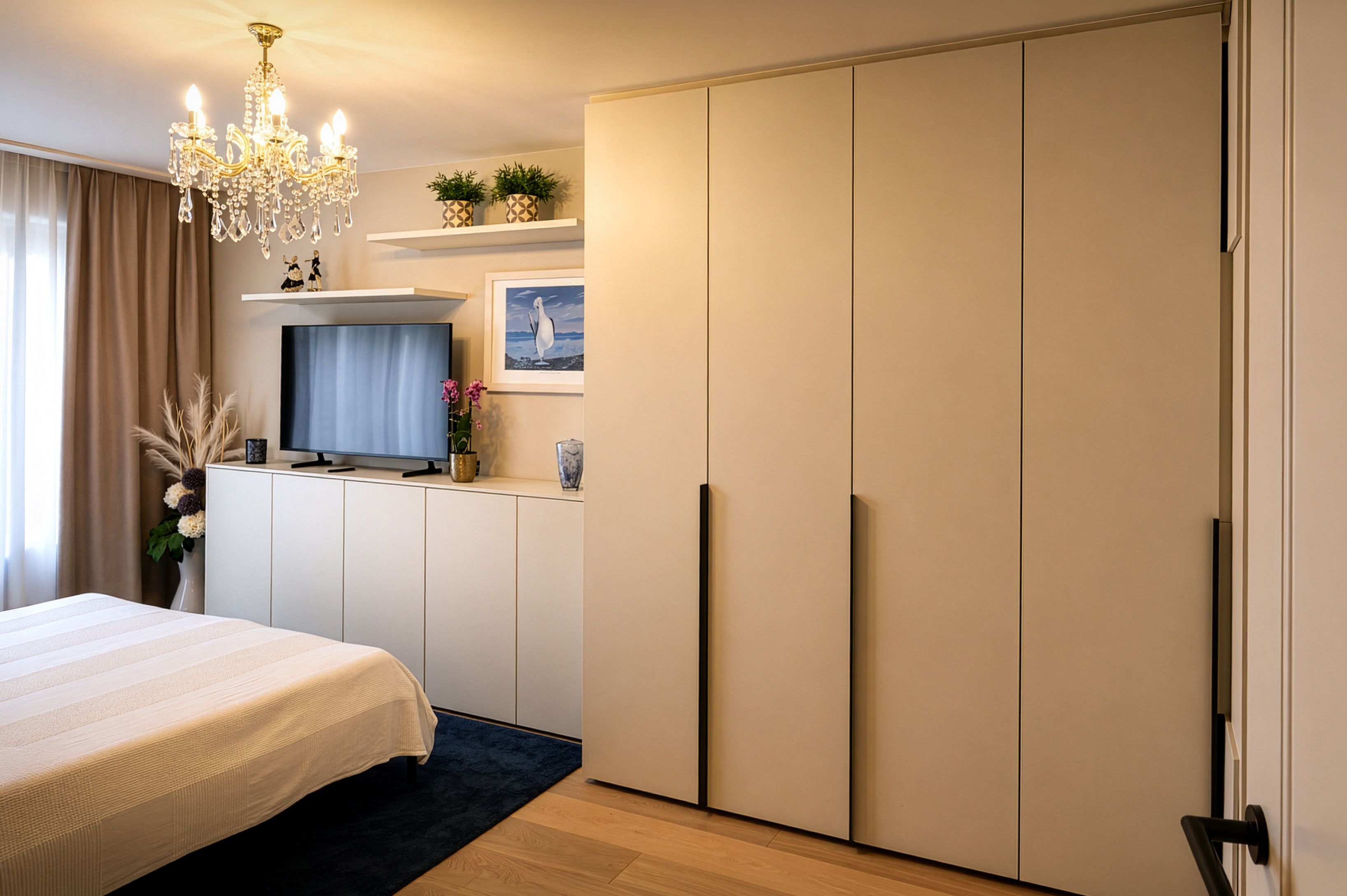 Ein Schlafzimmer mit Bett, Flachbildfernseher, Kronleuchter und weißen Schiebetüren. Der Raum hat einen Holzboden und eine weiße Wand.