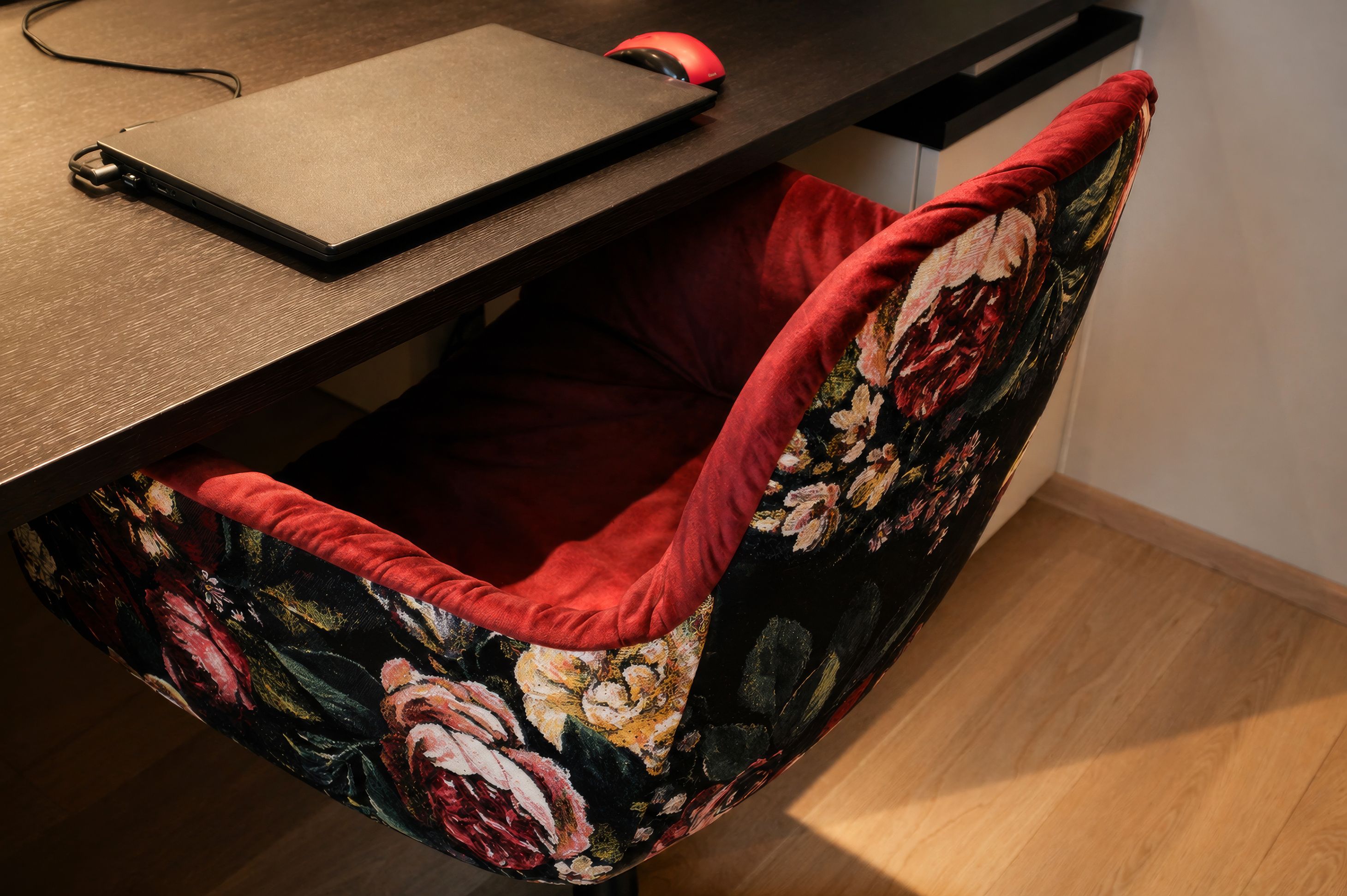 Eine Nahaufnahme eines Stuhls mit einem Blumenmuster auf Sitz und Rückenlehne. Ein Laptop liegt auf einem hölzernen Schreibtisch über dem Stuhl.