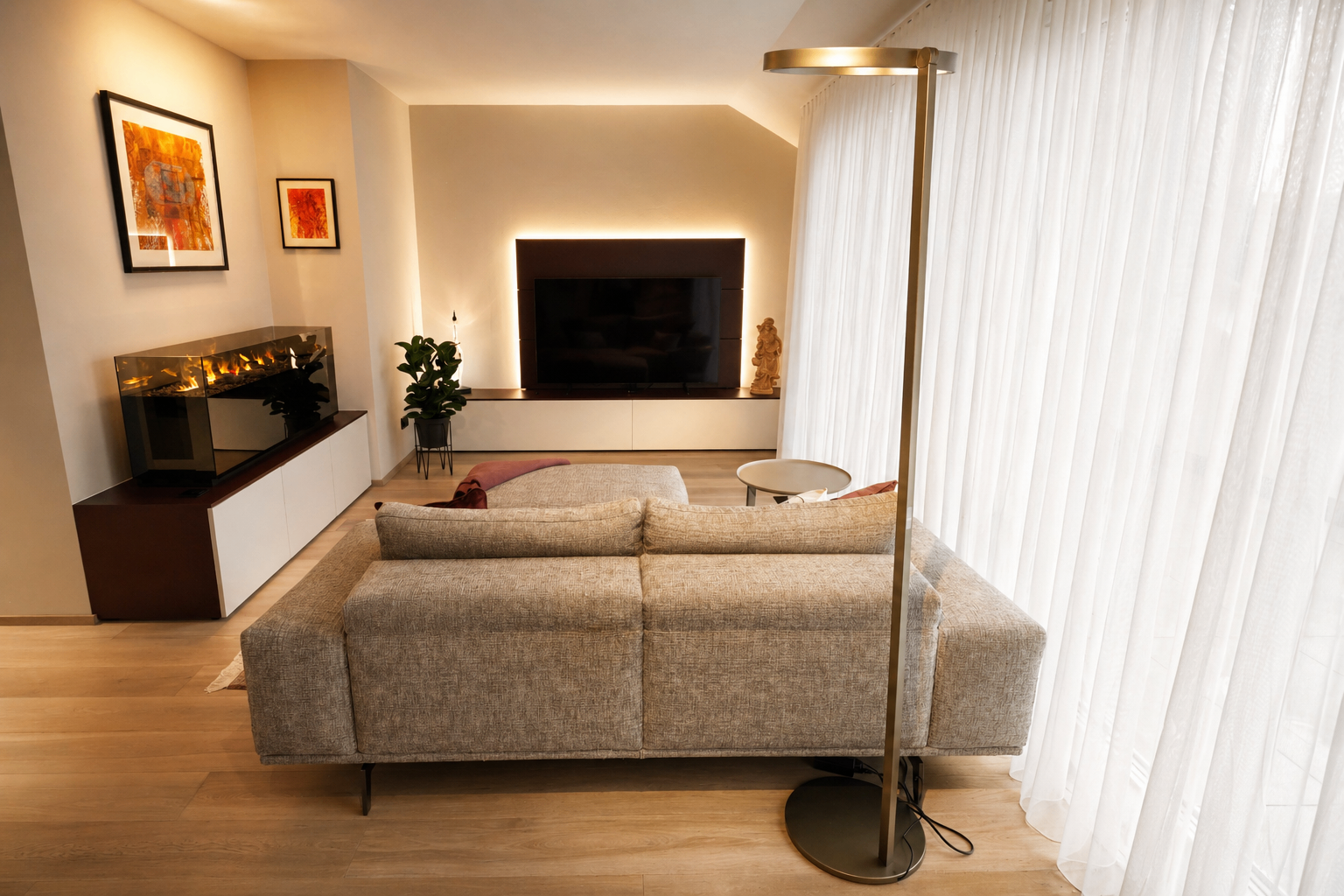 Ein modernes Wohnzimmer mit einem beigen Sofa, einem großen Fernseher, einer weißen Wand und einem weißen Vorhang. Daneben steht ein hoher Stehleuchte neben dem Sofa.