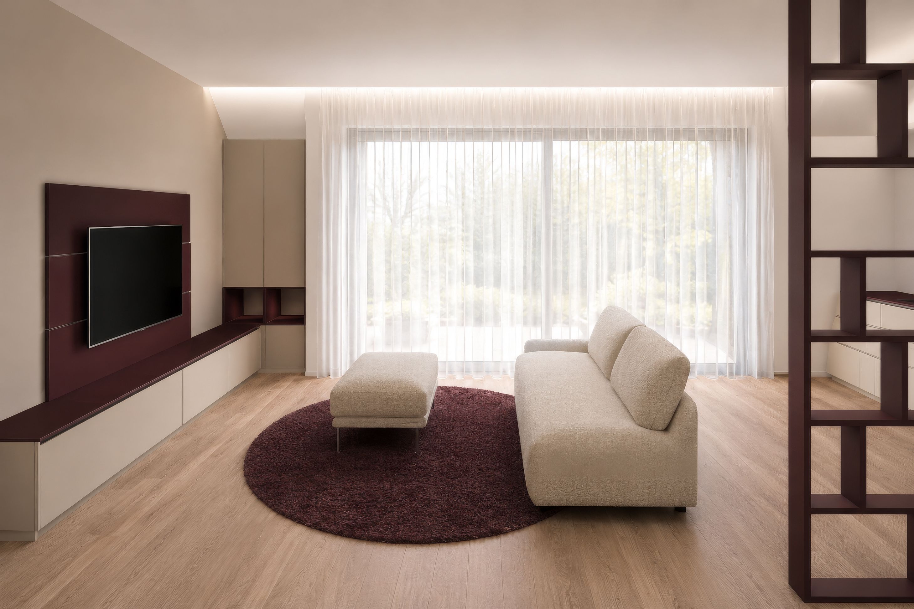 Modernes Wohnzimmer mit weißen Möbeln, beiger Couch, braunem Ottomane und rundem Teppich. Großes Fenster mit weißen Vorhängen. Entertainment-Center und Flachbild-TV. Holzboden.