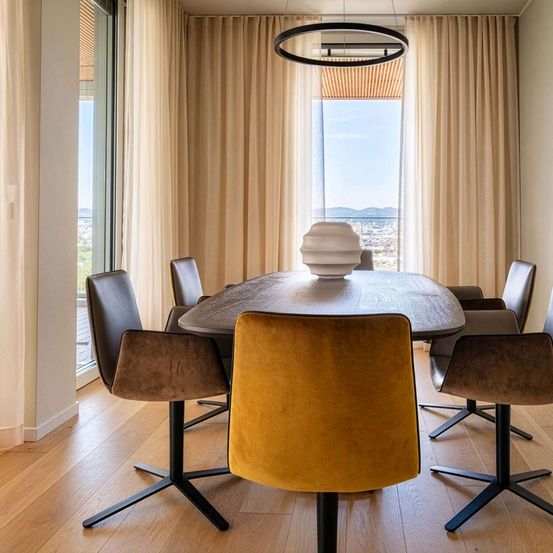 Ein elegant gestaltetes Esszimmer mit einem Holztisch, Lederstühlen und großen Fenstern, die einen Blick auf die Stadtlandschaft bieten.