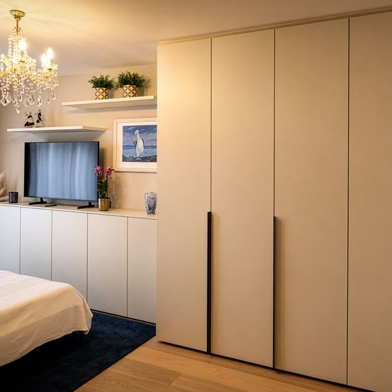 Ein Schlafzimmer mit weißen Schränken, einem Fernseher auf einem Regal, einer Kristallleuchte und einem Bild eines Pinguins an der Wand.